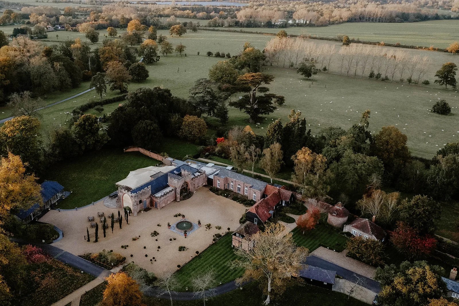 Autumn aerial view of Wasing Park, the courtyard and gardens framed by trees with the estate parkland stretching away, Wasing Park Weddings