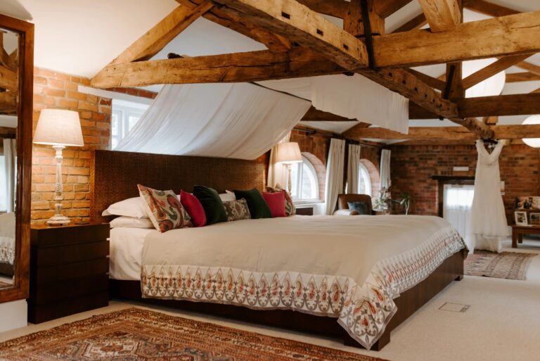 The Honeymoon Suite in the former hayloft: exposed beams, brick walls and a large bed under a draped canopy, Wasing Park Weddings