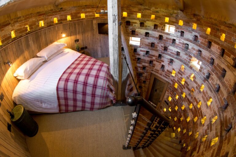The Dovecote suite from above, a bed beneath the curved brick wall of old nesting boxes lit with small lights, Wasing Park Weddings