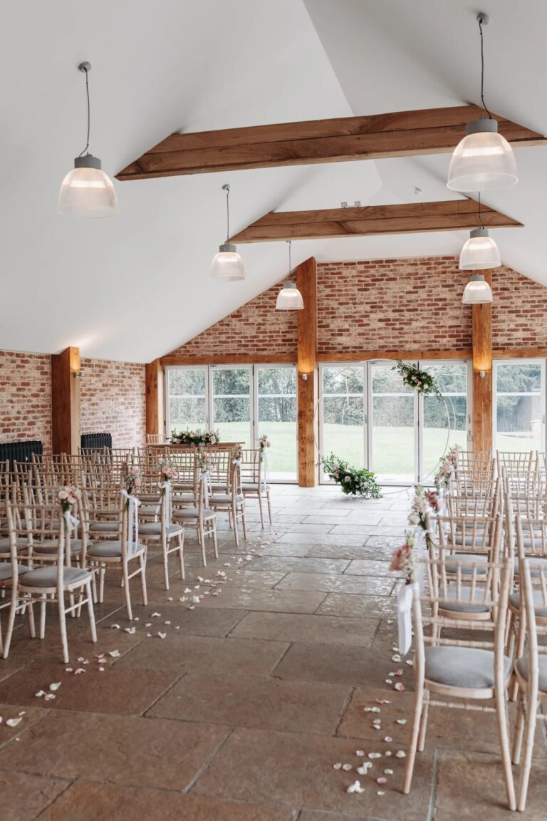 The Garden Room set for a civil ceremony, with an aisle between white chairs leading to glass doors onto the garden, Wasing Park Weddings
