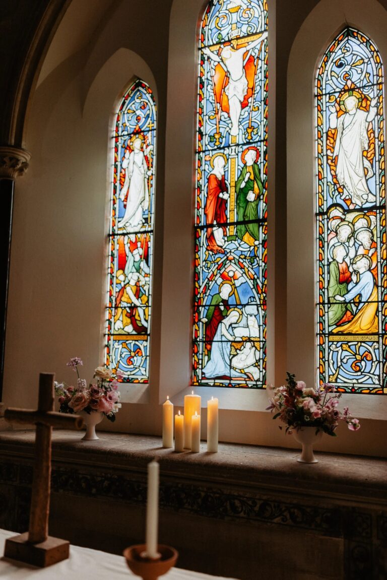 Stained-glass windows above candles and flowers on the altar of St Nicholas Church, Wasing Park Weddings