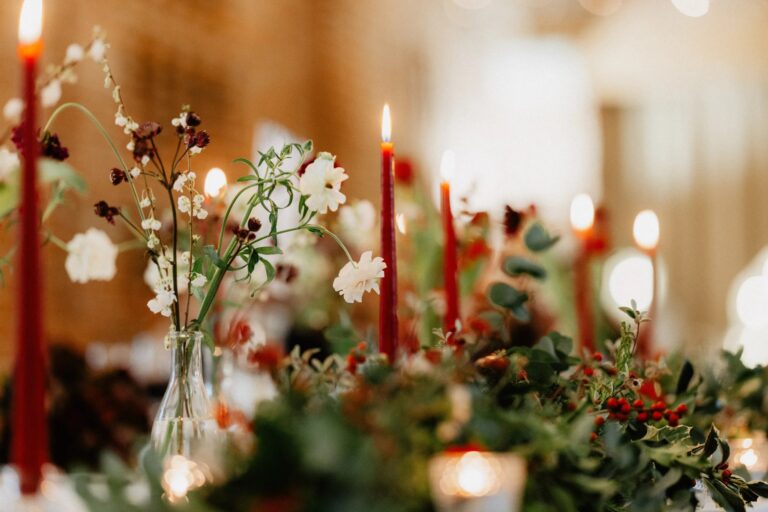 A winter table detail with tall red candles, white flowers, holly and berries, Wasing Park Weddings