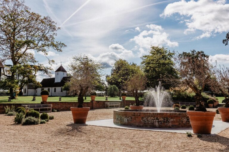 The courtyard fountain and potted olive trees, with the white turret of St Nicholas Church behind, Wasing Park Weddings