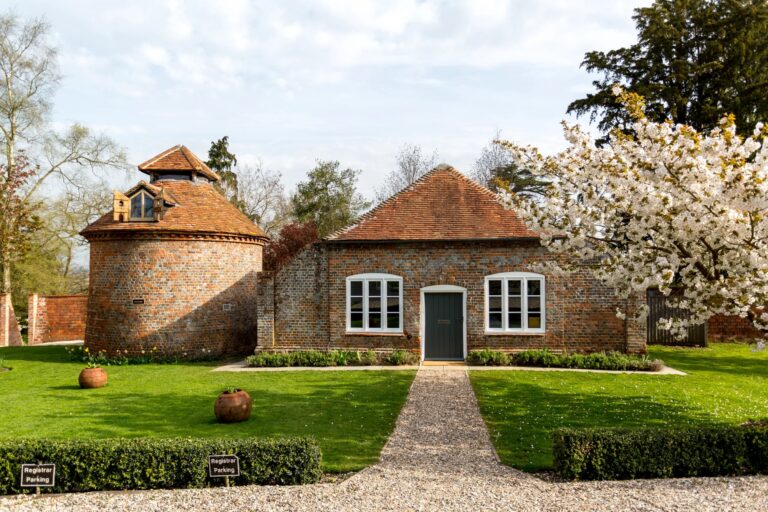 The round brick Dovecote beside the Smithy cottage, with a blossom tree and lawns in spring, Wasing Park Weddings
