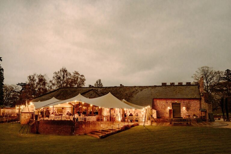 The Castle Barn and its terrace tent glowing at night during an evening reception, Wasing Park Weddings