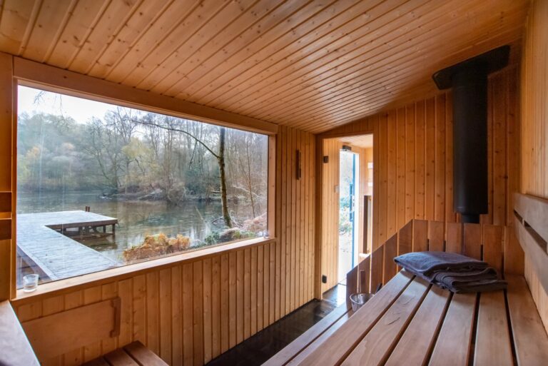 Inside the wood-fired sauna, timber benches and a panoramic window looking onto the lake and jetty, Wasing Park Weddings