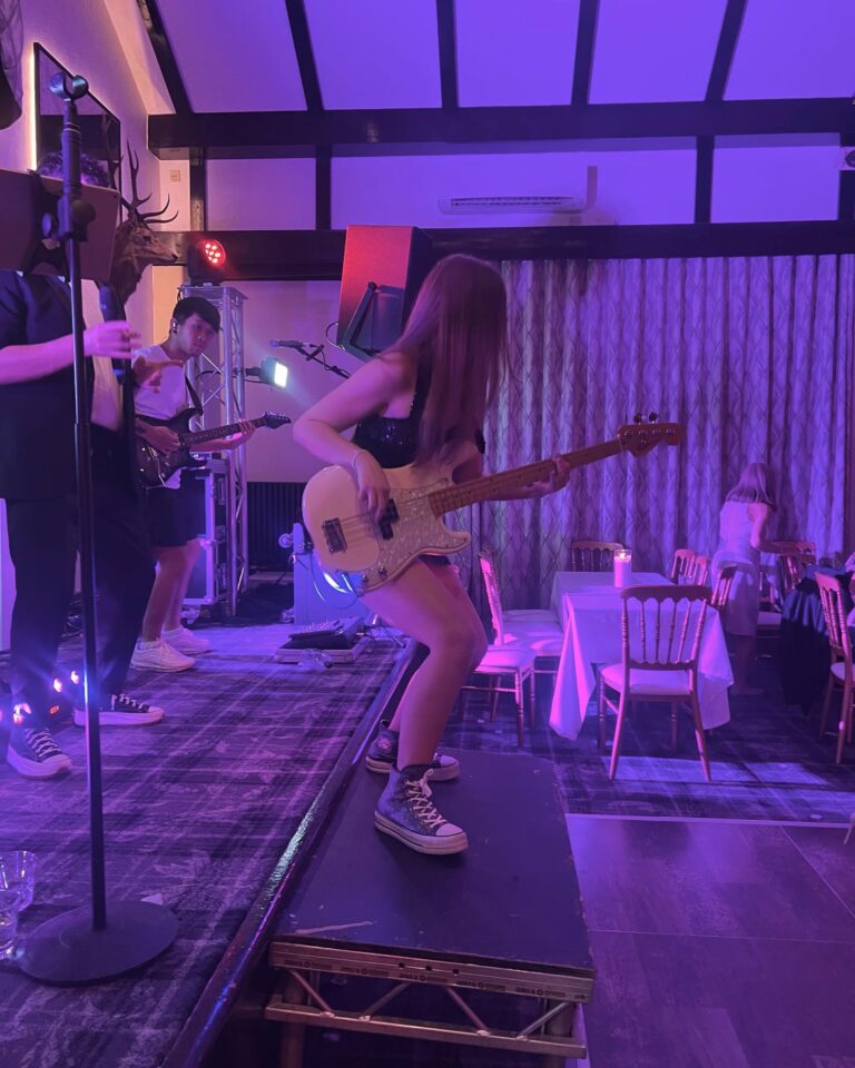 A bass player performing on a raised platform in a purple-lit room, Waterfront