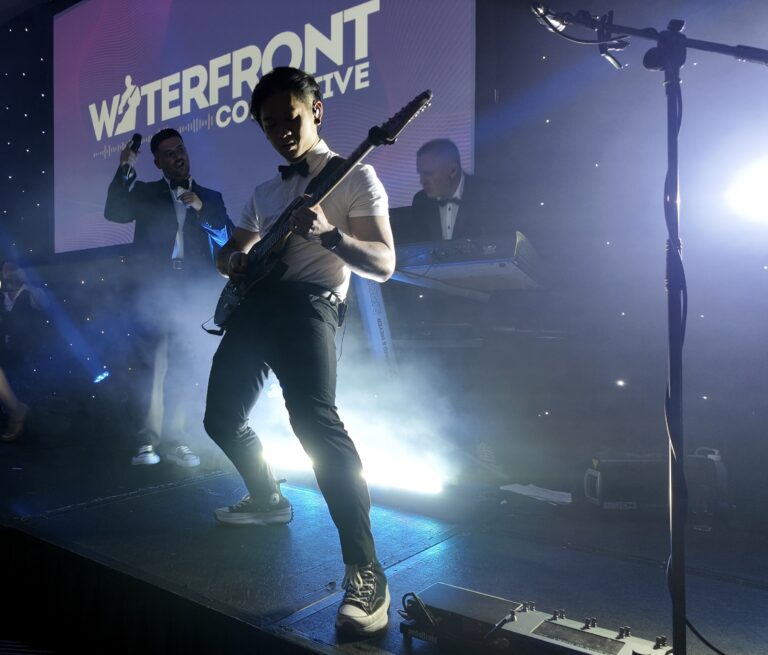 A guitarist in front of a screen carrying the band name, Waterfront
