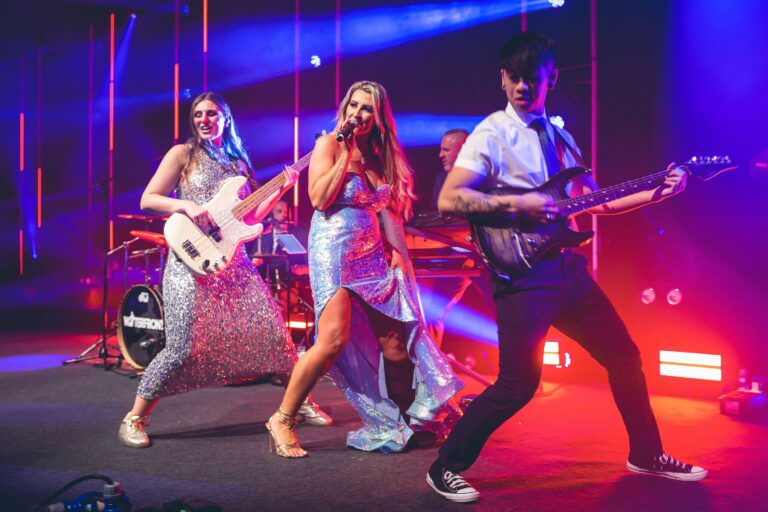 Three performers on stage under red and blue lighting, Waterfront