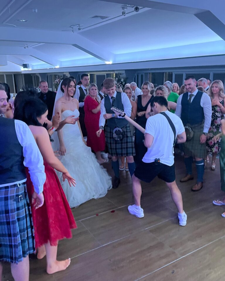 A bride and a groom in a kilt dancing among guests, Waterfront