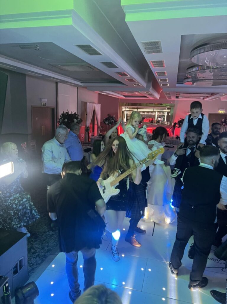 Guests dancing on a lit floor with a guitarist among them, Waterfront