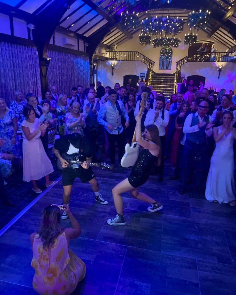 A guitarist playing among guests on the dance floor of a timber-framed room, Waterfront