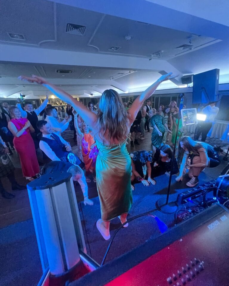 A guest dancing with arms raised on the stage platform as the room dances, Waterfront