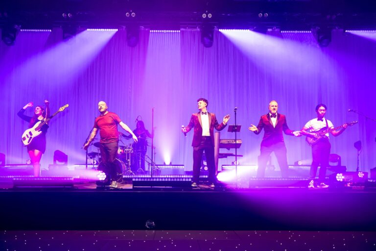 The full band on stage with purple and white lighting, Waterfront