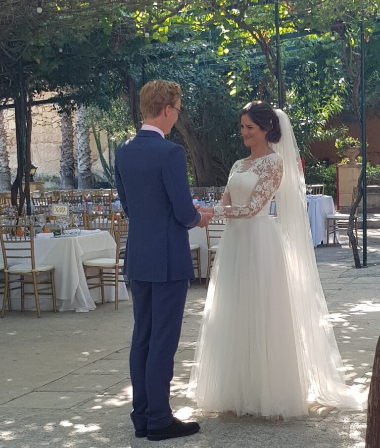 Couple exchanging vows in a vine-covered courtyard set for dinner, Wed In Malta