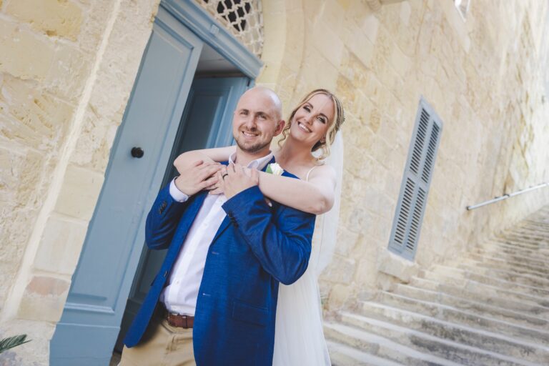 Couple embracing on limestone steps beside a pale blue door, Wed In Malta