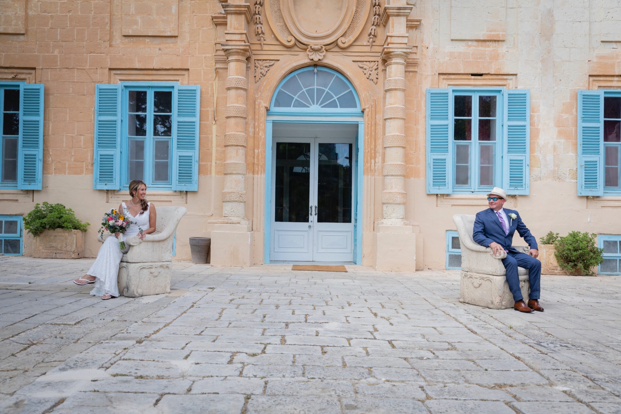 Couple seated apart in a palazzo courtyard with pale blue shutters, Wed In Malta