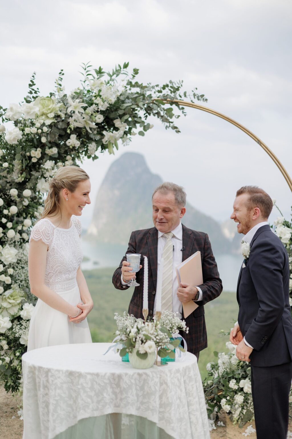 A white floral ring arch ceremony with limestone karst behind, Phang Nga