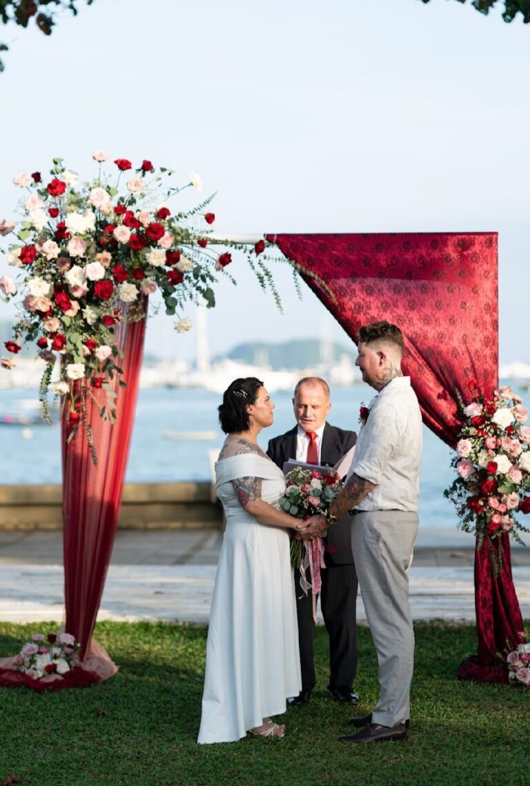 Ceremony under a red draped arch with roses beside a marina, Wedding Celebrant Phuket - Paul Cunliffe