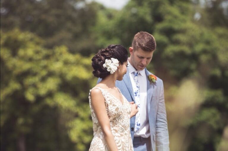 A bride and groom in a garden, a white flower pinned in her hair, groom in a pale blue suit, Wedding Hair And Makeup By Lisa
