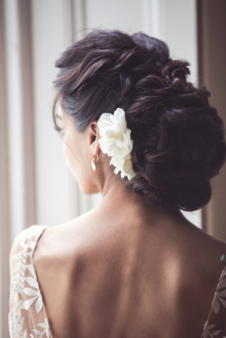 A twisted updo finished with a white flower behind the ear, a lace cap-sleeve gown, Wedding Hair And Makeup By Lisa