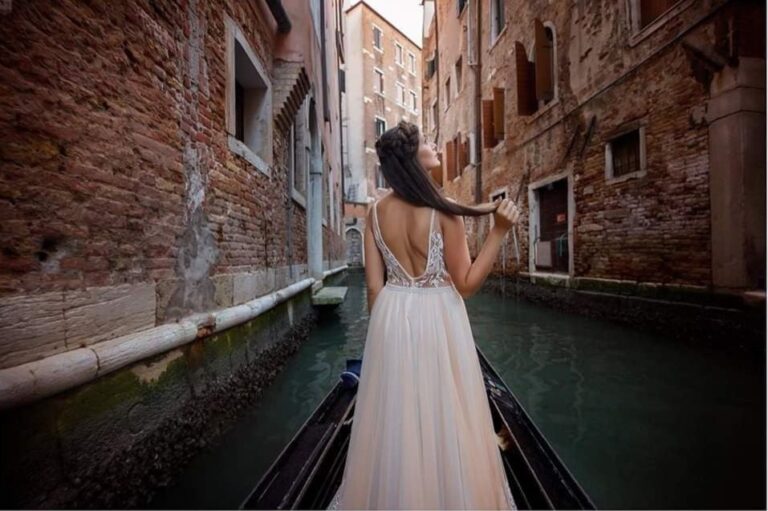 A bride in a lace gown looks back from a gondola on a Venice canal at dusk, Wedding Hair And Makeup By Lisa