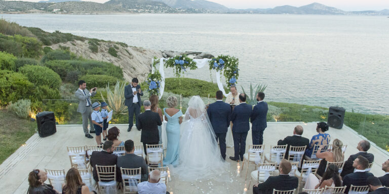 A ceremony on a terrace above the sea with guests seated in rows, Wedding in Greece