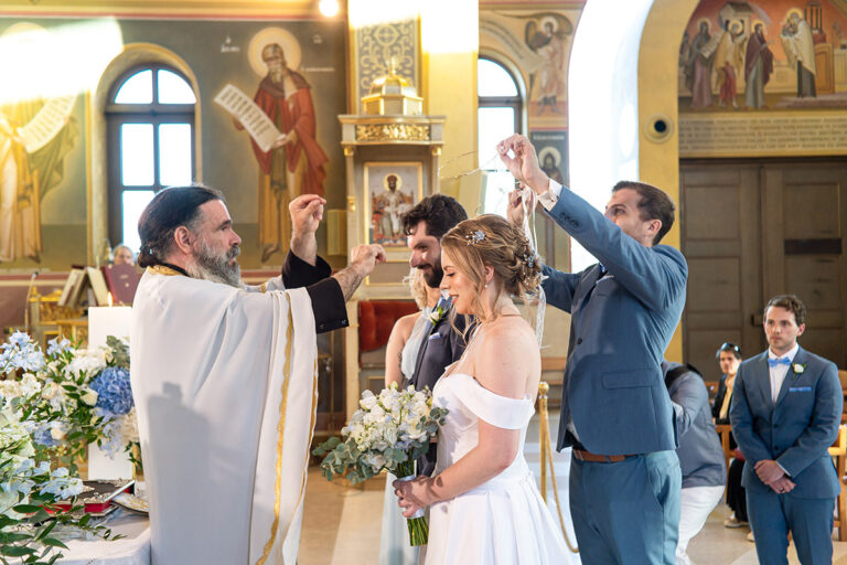 The priest crowns the couple in a church dressed with blue and white flowers, Wedding in Greece