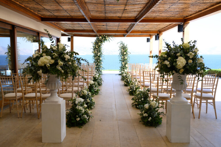 A ceremony aisle lined with white flowers and greenery under a timber pergola, Wedding in Greece