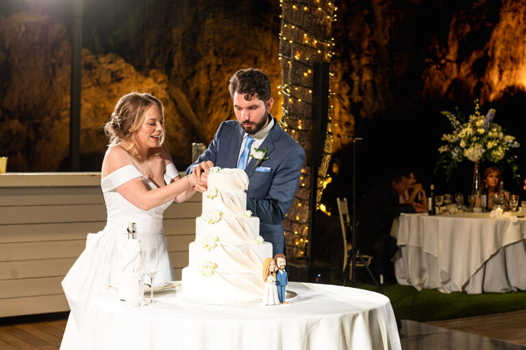 A bride and groom cut a tiered white cake in a lit room, Wedding in Greece