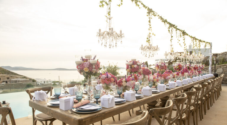 Crystal chandeliers hang over a long banquet table of pink roses, Wedding in Greece