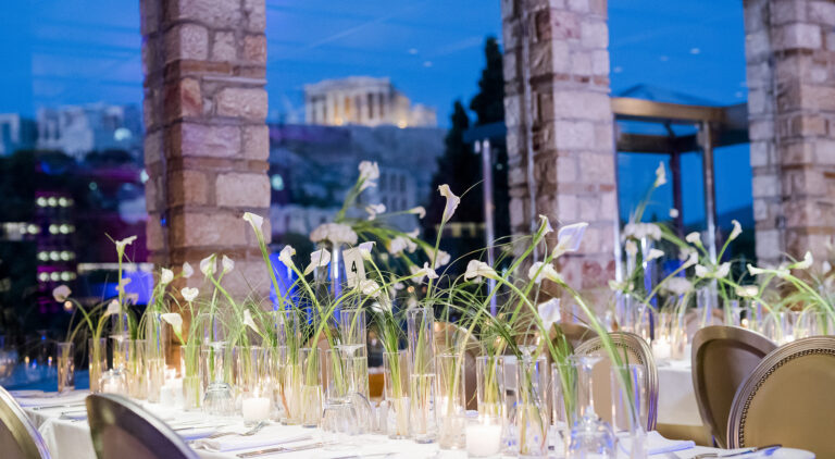 A reception table of tall glass vases with the Acropolis behind, Wedding in Greece