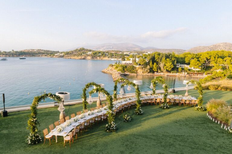 Arches of greenery over a long banquet table on a lawn beside the bay, Wedding in Greece