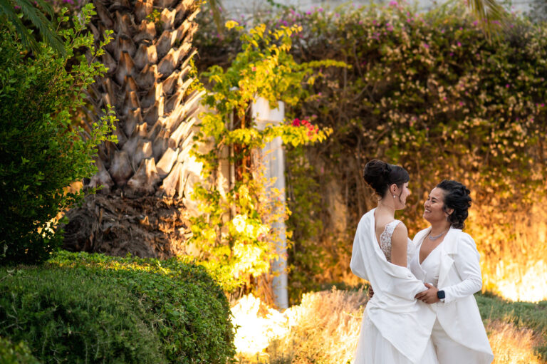 Two brides together in a garden lit with warm lights at dusk, Wedding in Greece