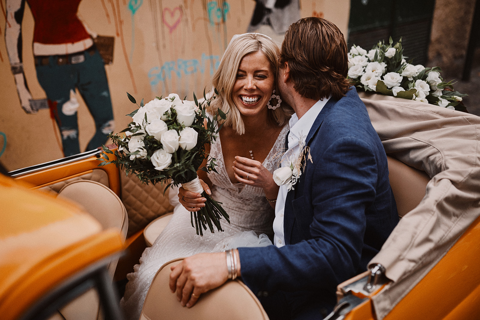 Couple laughing in the back of the yellow Fiat 500 with a white bouquet, Wedding In Yellow Vintage