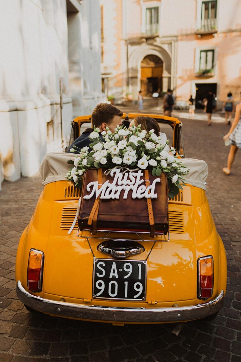 Rear of the Fiat 500 with Just Married sign and white flowers outside a church, Wedding In Yellow Vintage