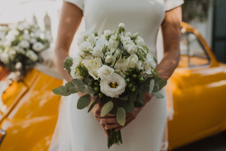 Bride holding a white ranunculus bouquet beside the yellow car, Wedding In Yellow Vintage