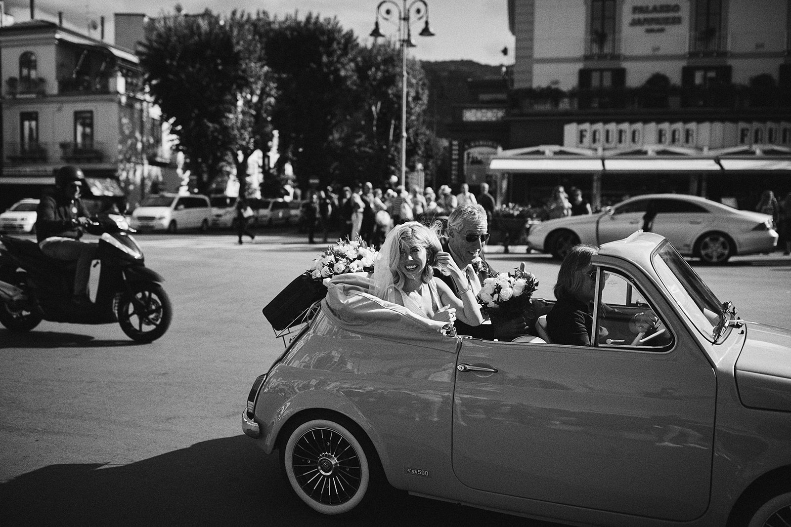Bride and groom driving through a piazza in the open Fiat 500, black and white, Capri, Wedding In Yellow Vintage