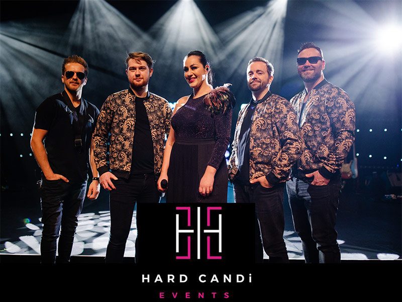 A five-piece band in patterned jackets on stage under spotlights