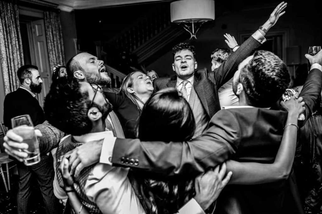 Guests with their arms raised on a crowded dance floor, in black and white