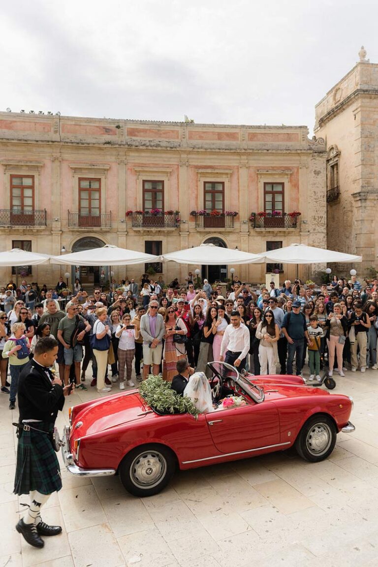 Bride arriving in a vintage red car in a crowded piazza, Wedding Sicily
