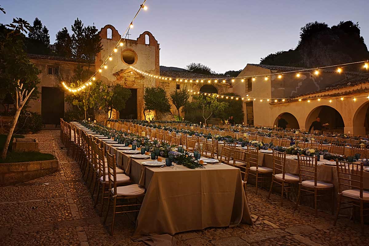 Long banquet tables under string lights in a stone courtyard at dusk, Sicily, Wedding Sicily
