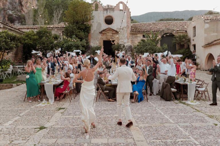 Guests waving napkins as the couple enter a courtyard reception, Wedding Sicily
