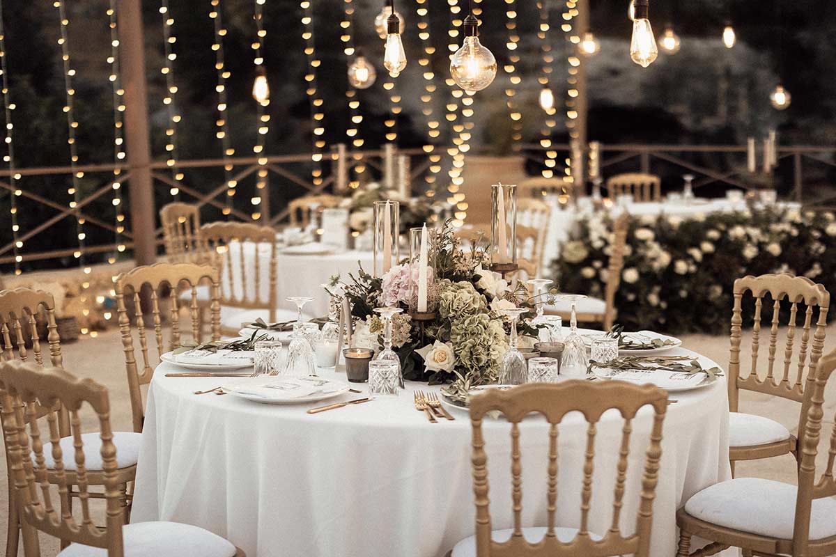 Round tables with gold chairs beneath hanging lights and a canopy of bulbs, Wedding Sicily