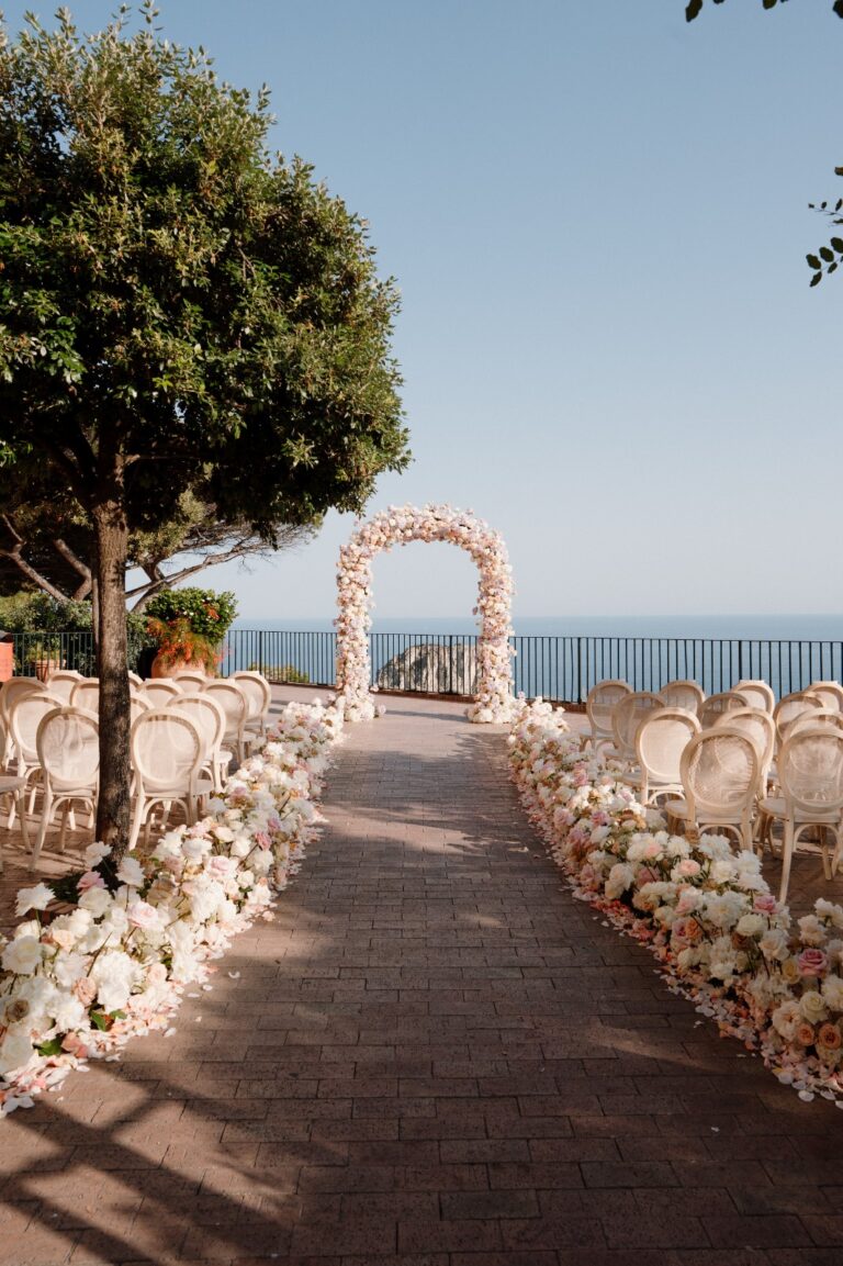 A ceremony aisle lined with white flowers leading to a floral arch at the cliff edge, Punta Tragara, Capri, Weddings Amalfi