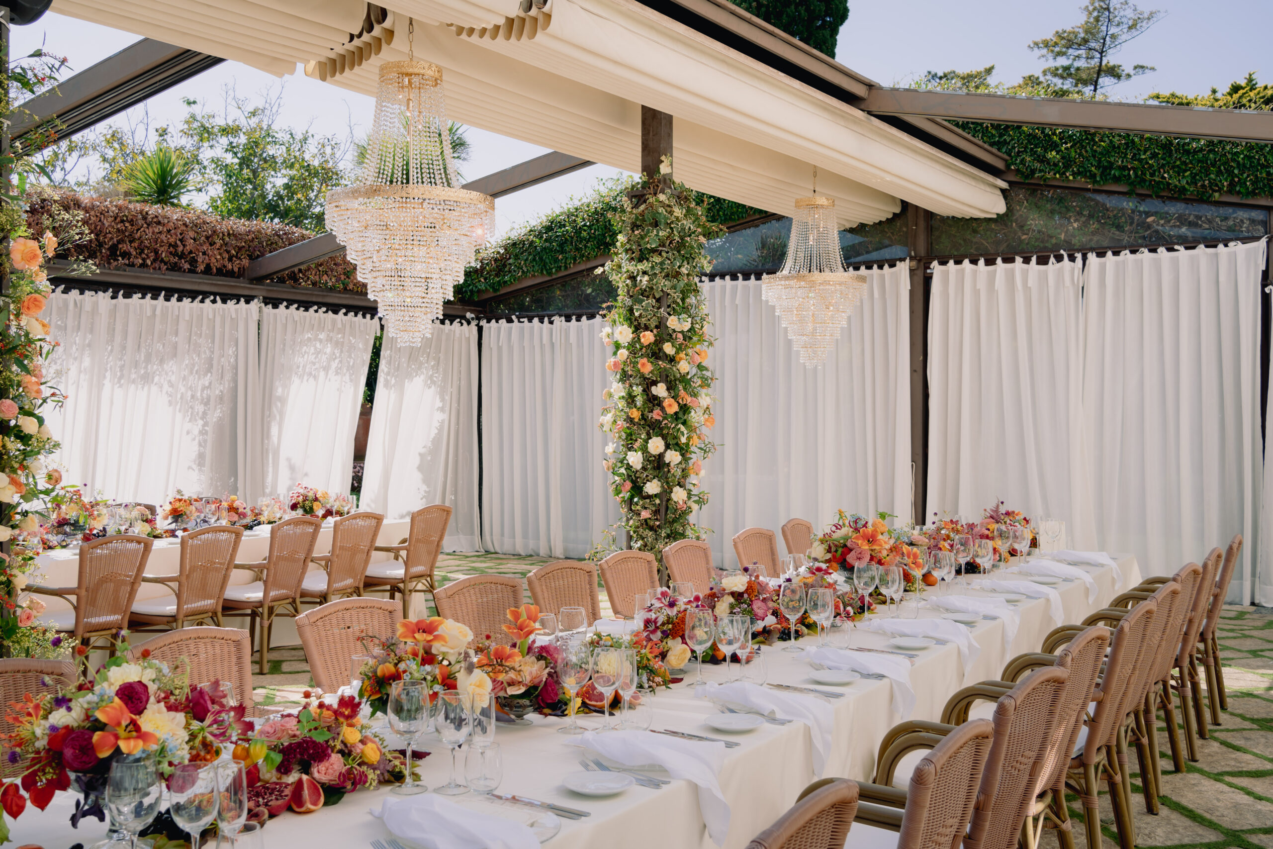 One long table under two crystal chandeliers in a white-draped pavilion, low bands of orange and pink flowers down the centre, Weddings Amalfi