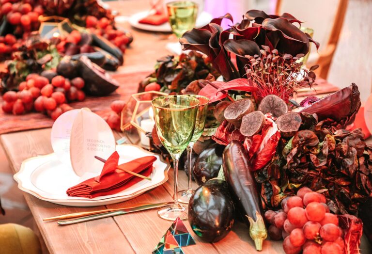A place setting among aubergines, red grapes, calla lilies and dark foliage on a wooden table, Weddings Amalfi