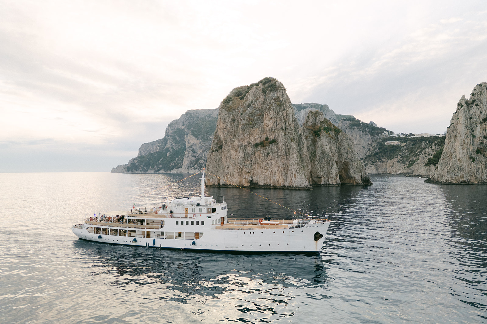 A white motor yacht at anchor off the Faraglioni rocks, Capri, in evening light, Weddings Amalfi