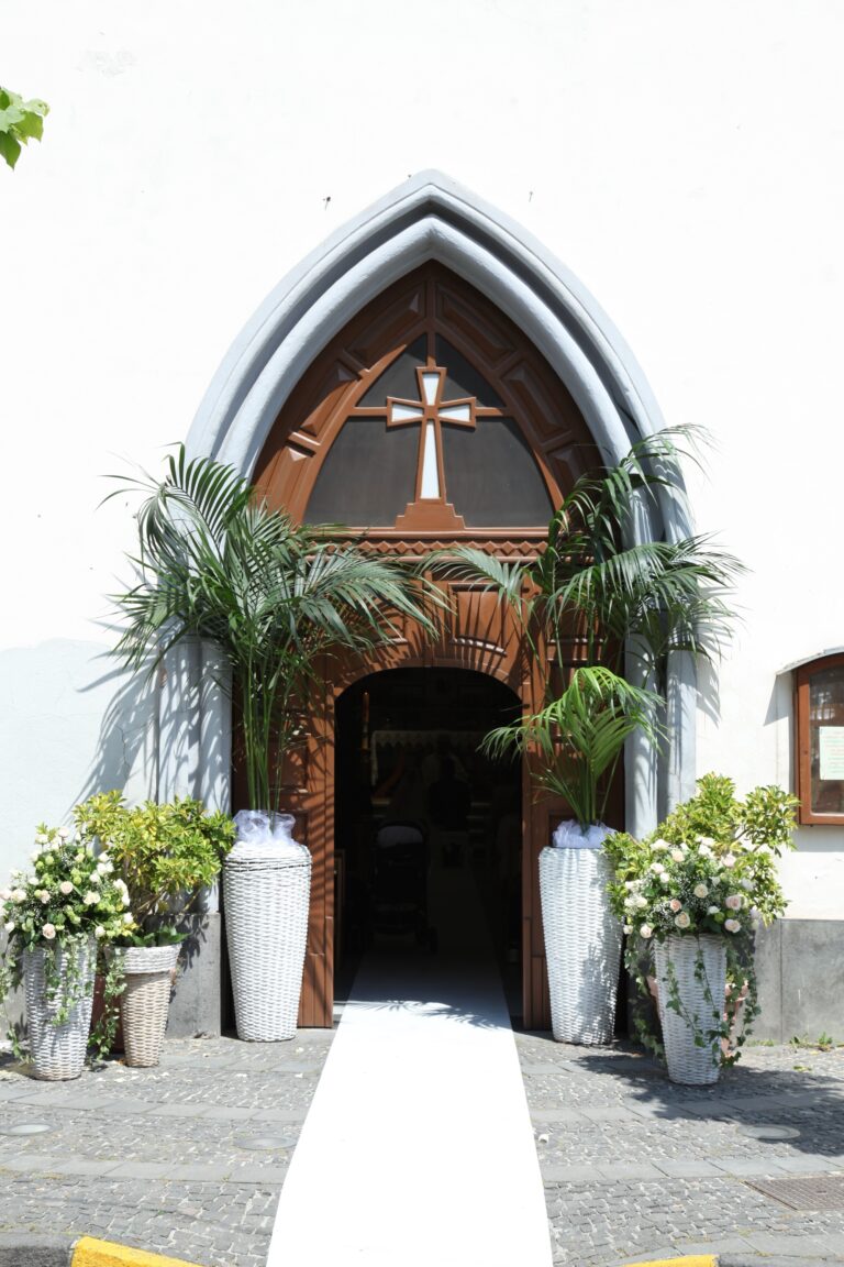A Gothic church doorway dressed with palms, white hydrangea and a white carpet, WEM Eventi
