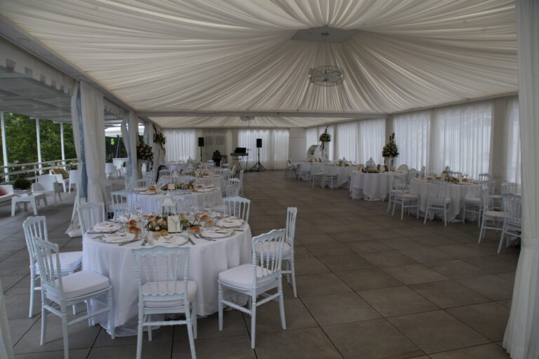 A draped white marquee laid with round tables and white chairs for the wedding dinner, WEM Eventi
